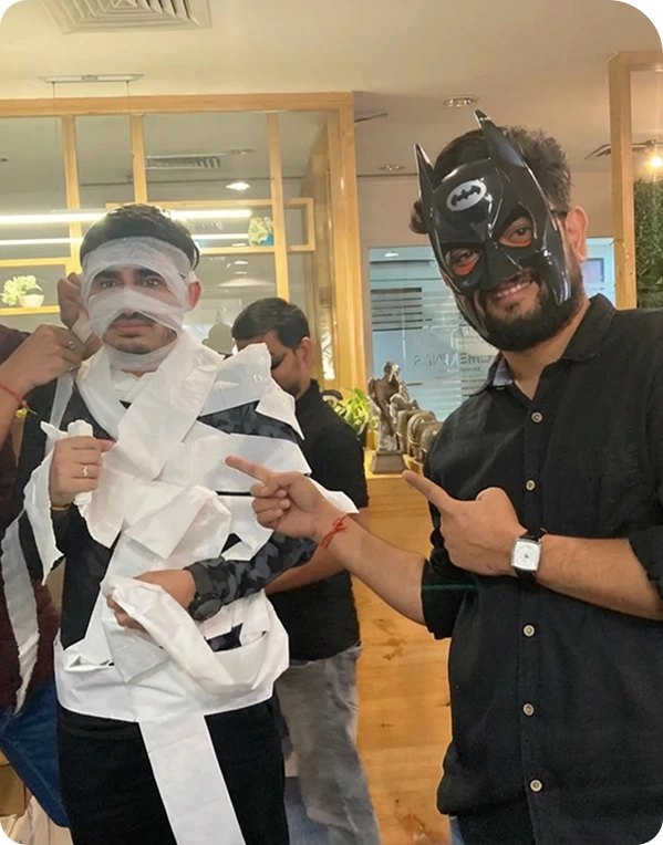 Employees having fun dressing up for a Halloween event, with one person wrapped as a mummy and another wearing a superhero mask