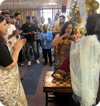 A Diwali festive celebration in the office, with employees gathered around a cake and clapping to celebrate an occasion.